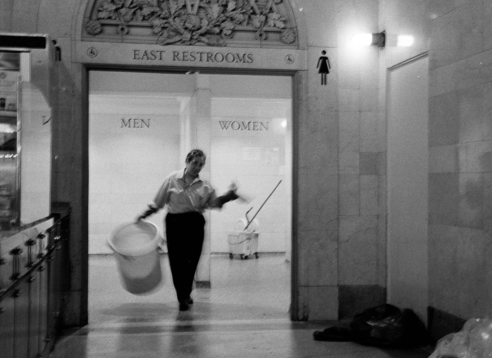 custodian leaving restroom carrying a trash bin