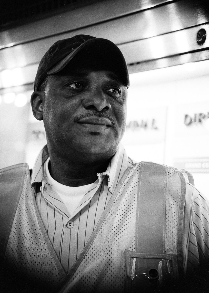 portrait of custodial man with striped shirt, hat and safety vest looking past the camera