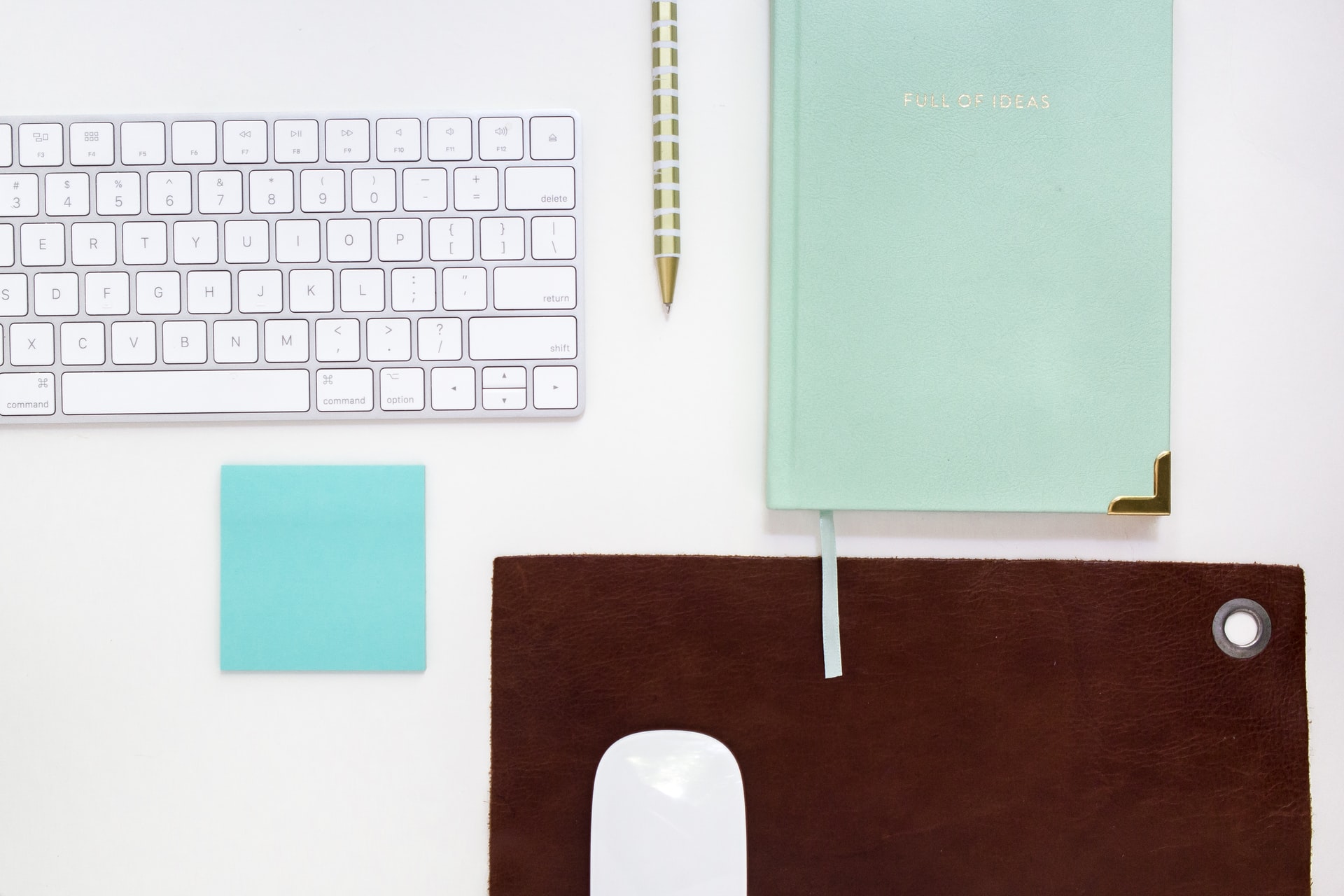 white keyboard with notebook, sticker, pencil, and mouse next to it on a white desk