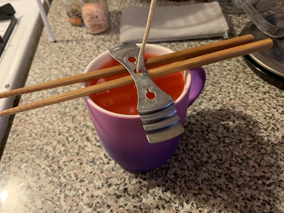 photo of the candle full of wax and 2 chopsticks being used to prop up a metal wick holder