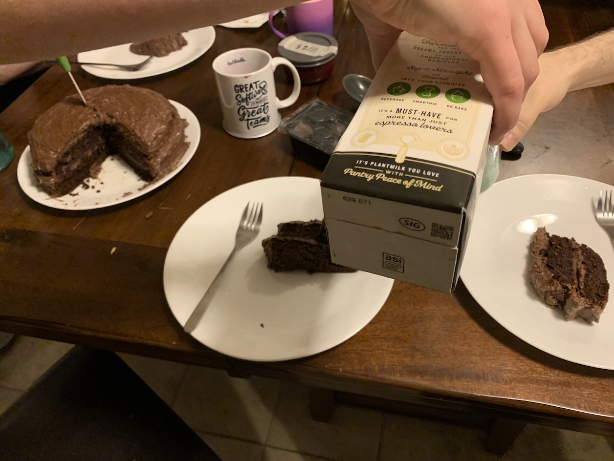 photo of my kitchen table and phil's pouring andy milk right in front of me. behind the arms are plates with slices of chocolate cake and the entire cake off to the side and kind of blurry
